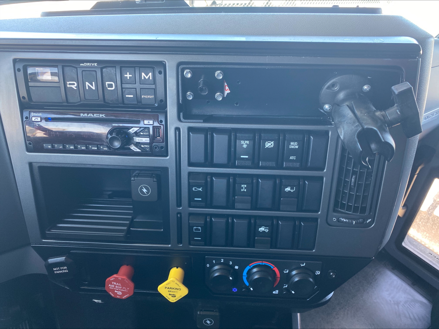 Dashboard of a Mack AN64T70 truck showing the gear selector with R N D P and M, radio unit, control buttons, power ports, and climate controls.