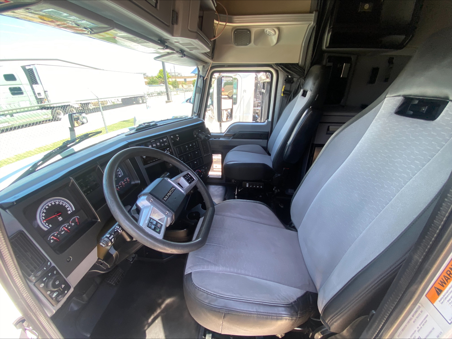 Truck cab interior showing steering wheel, dashboard, and driver and passenger seats in a Mack AN64T70 sleeper truck.