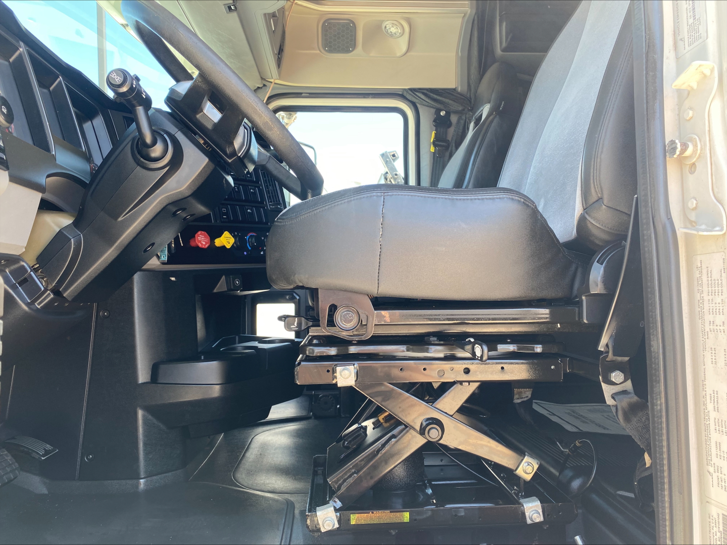Cab interior of a 2019 Mack AN64T70 truck showing driver seat and steering wheel with raised seat suspension mechanism visible