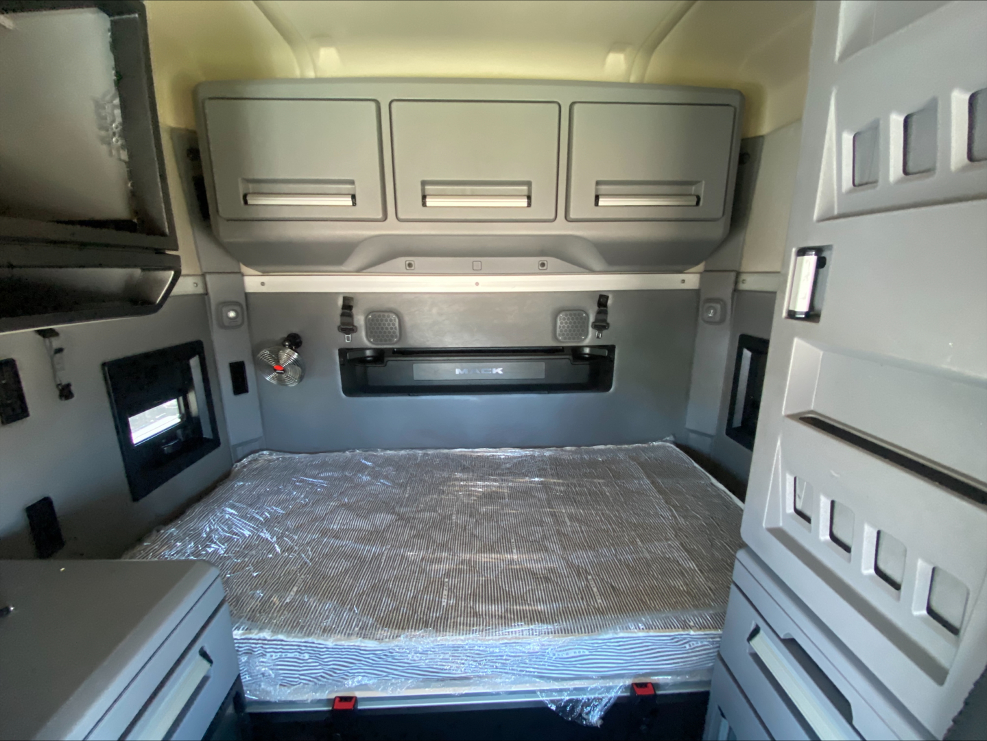 Truck sleeper cab interior showing rear storage cabinets and a wrapped mattress platform in a Mack AN64T70 sleeper