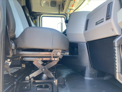 Truck interior cab view showing front driver seat with mechanical suspension under seat and dashboard area with vents and controls.