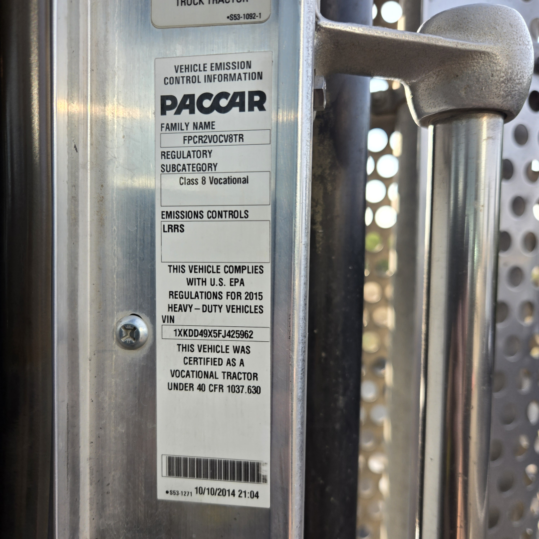 VIN plate on truck door shows vehicle emission controls label from PACCAR and text indicating vocational heavy-duty classification, 2015 Kenworth T800 listing information.