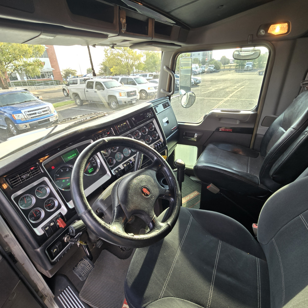 Kenworth T800 truck cab interior showing steering wheel, dashboard with gauges, driver seat, and passenger seat visible through open door.