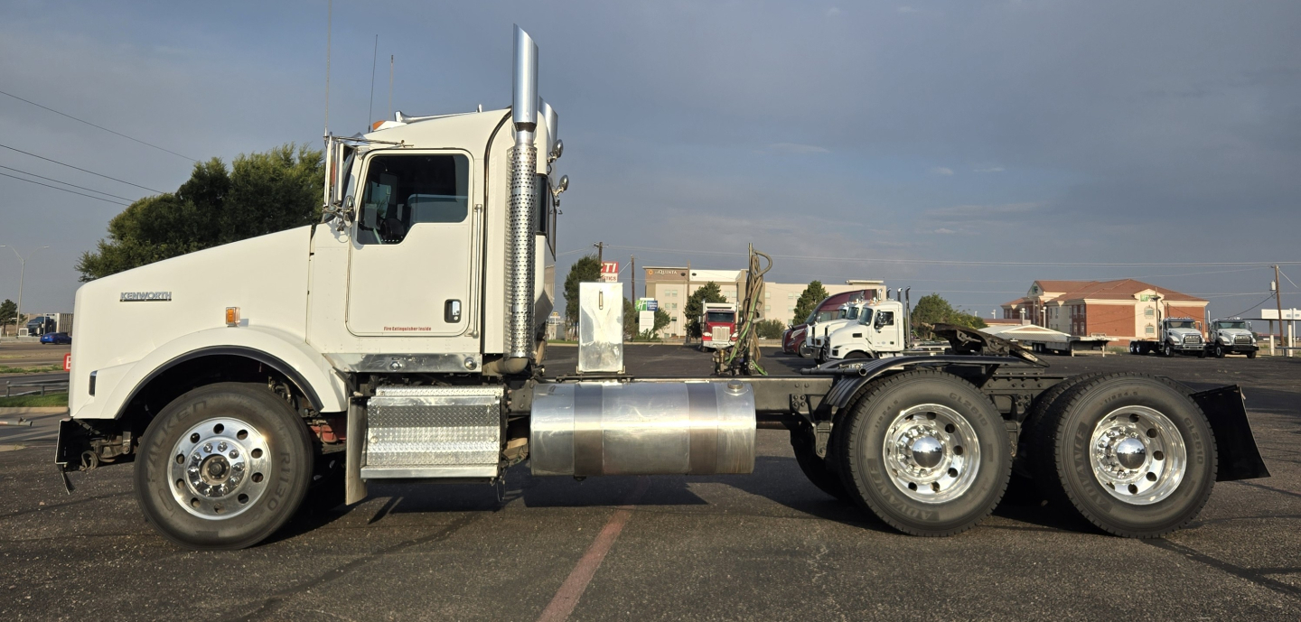 Kenworth T800 conventional daycab truck side view showing tandem rear axles and chrome fuel tank; white cab and sleeper panel, large vertical exhaust stacks.