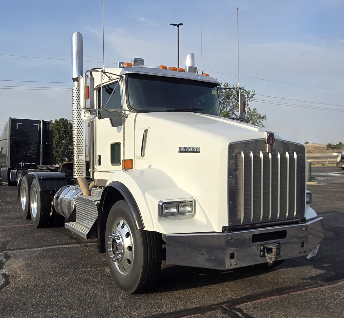 Kenworth T800 daycab truck front-left view showing chrome grille, dual exhaust stacks, and white cab with Kenworth emblem.