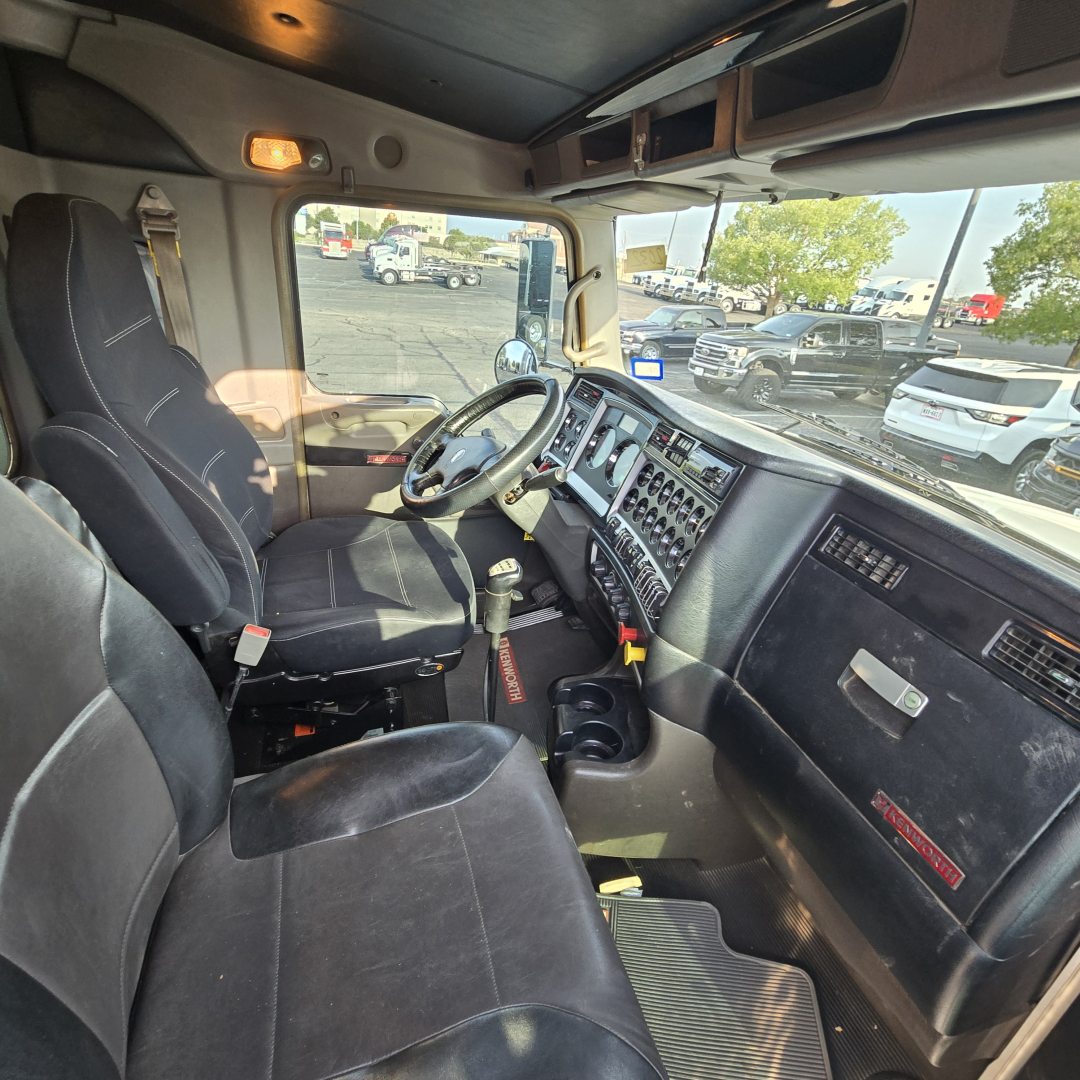 Kenworth T800 cab interior view showing driver seat and dashboard with control panels and steering wheel, VIN plate and gear shifter visible.