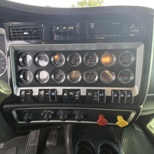 Dashboard of a 2015 Kenworth T800 showing multiple gauges, switches, and a radio unit; various labels on switches and circular gauge faces visible.