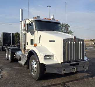 Kenworth T800 daycab truck front-left view showing chrome grille, dual exhaust stacks, and white cab with Kenworth emblem.