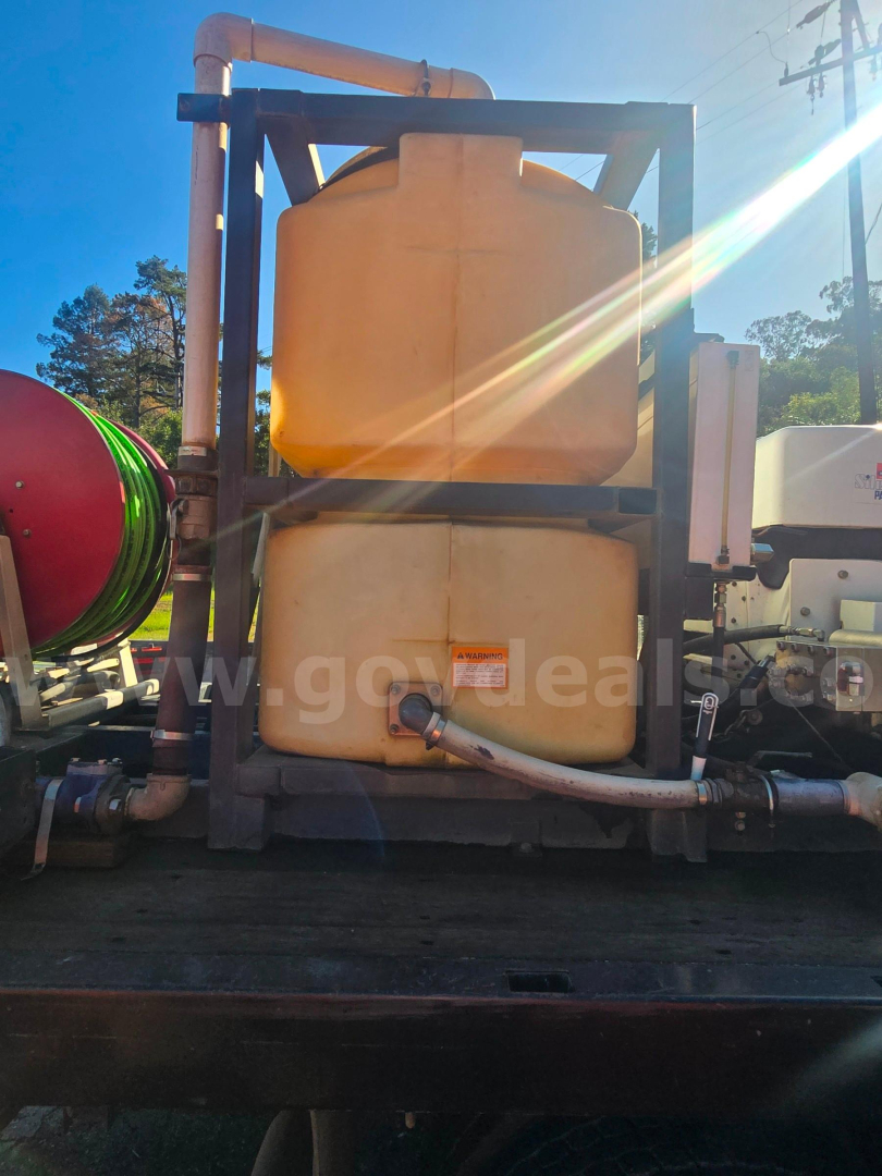 Fuel water separator tanks and pipes on a Ford F-450 truck equipment mount showing two stacked translucent yellow tanks with hoses and a side valve.