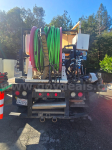 Rear view of a Ford F-450 utility truck with a large hose reel and tanks, hoses in green and purple, hydraulic components, and warning lights visible.