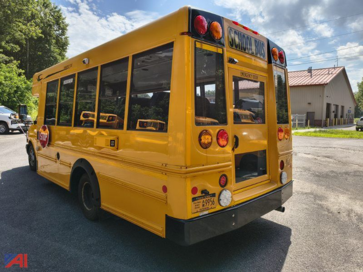 Rear-right view of a yellow school bus with open back door and windows, ‘SCHOOL BUS’ sign on rear, red tail lights, and inspection stickers visible.