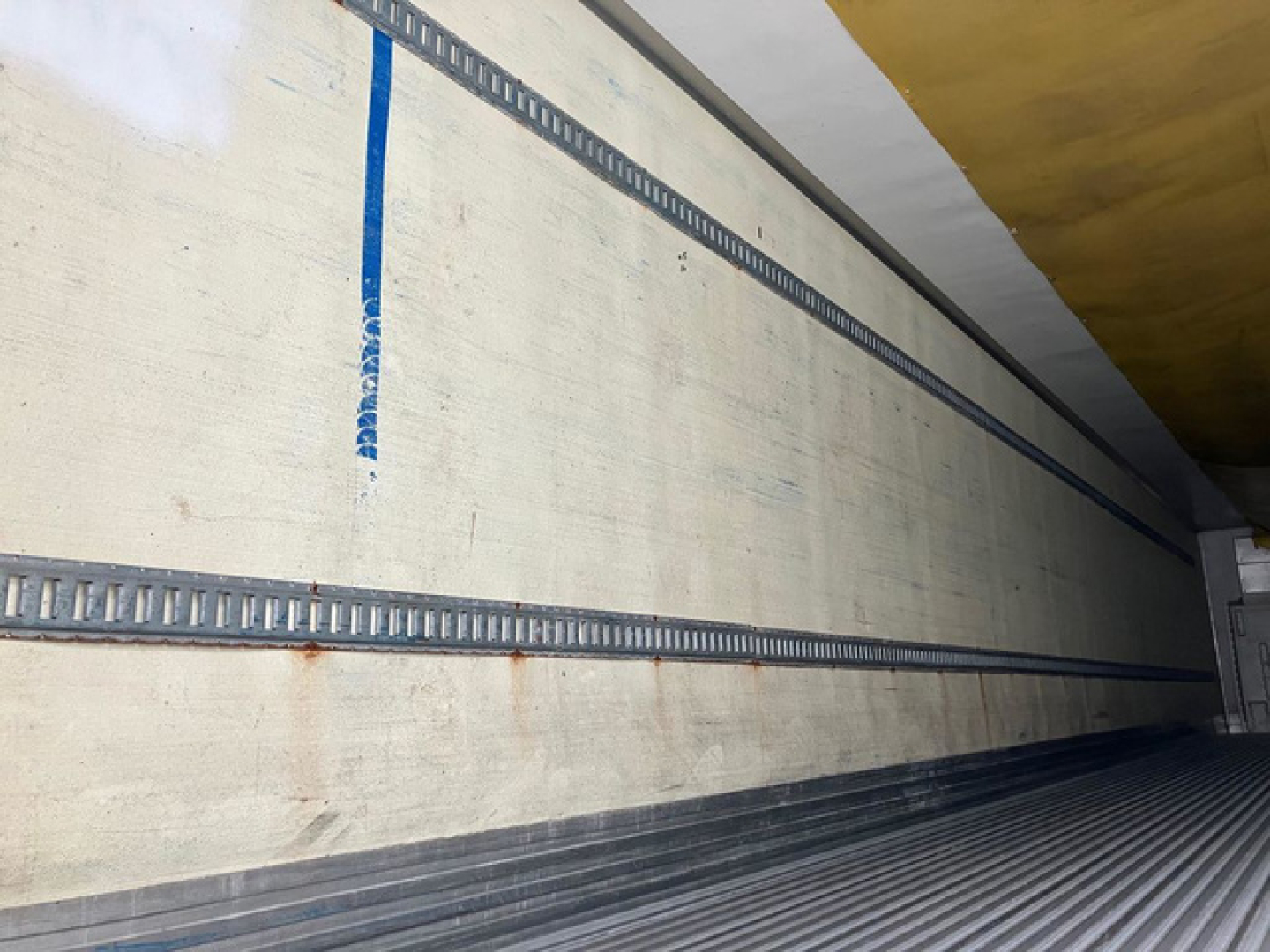 Trailer interior side wall with metal track rails and ribbed flooring in a refrigerated trailer.