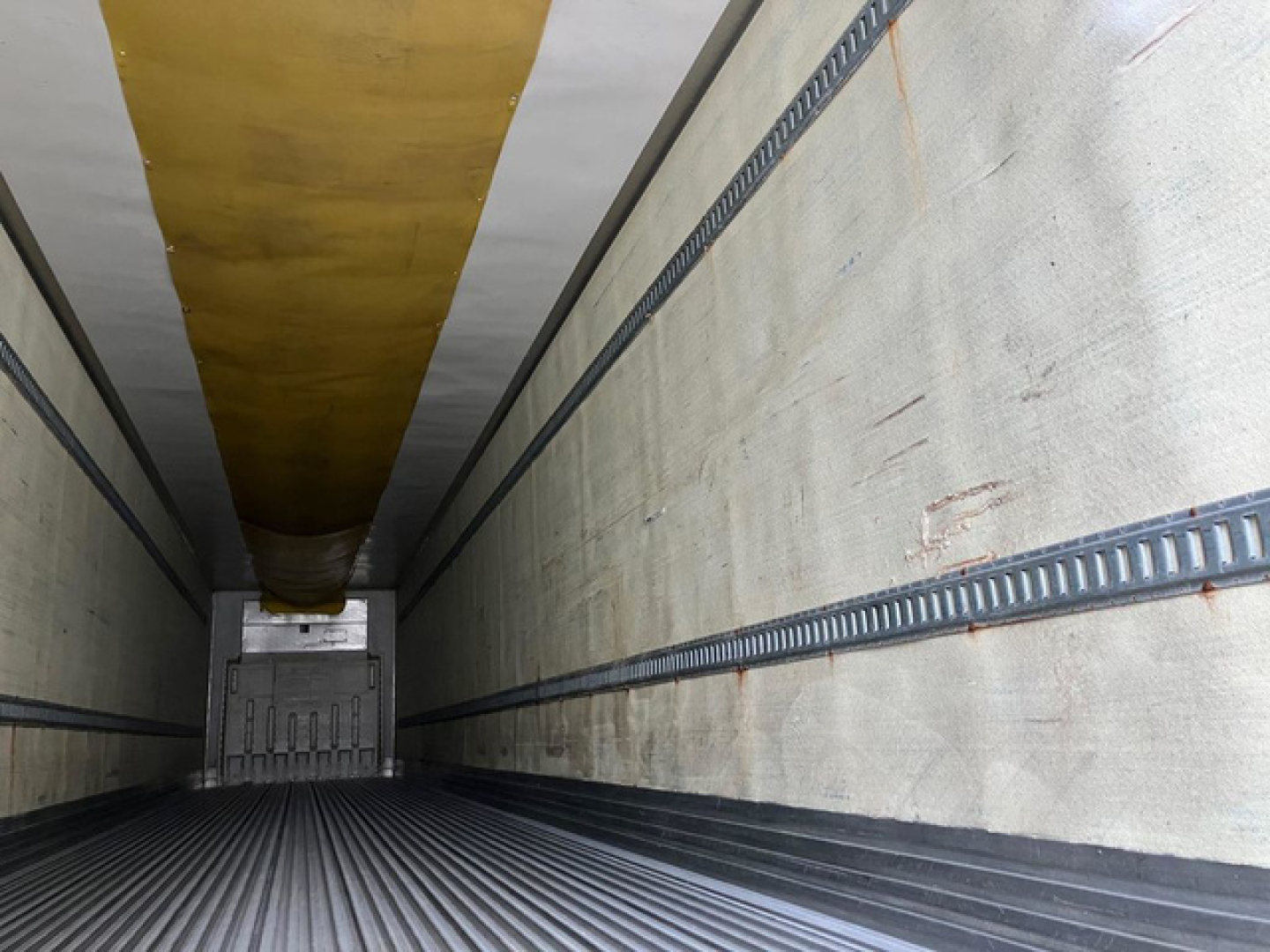 Trailer interior showing insulated sidewalls and floor, cargo area with reefer unit housing at rear, long yellow ceiling strip and side rails.