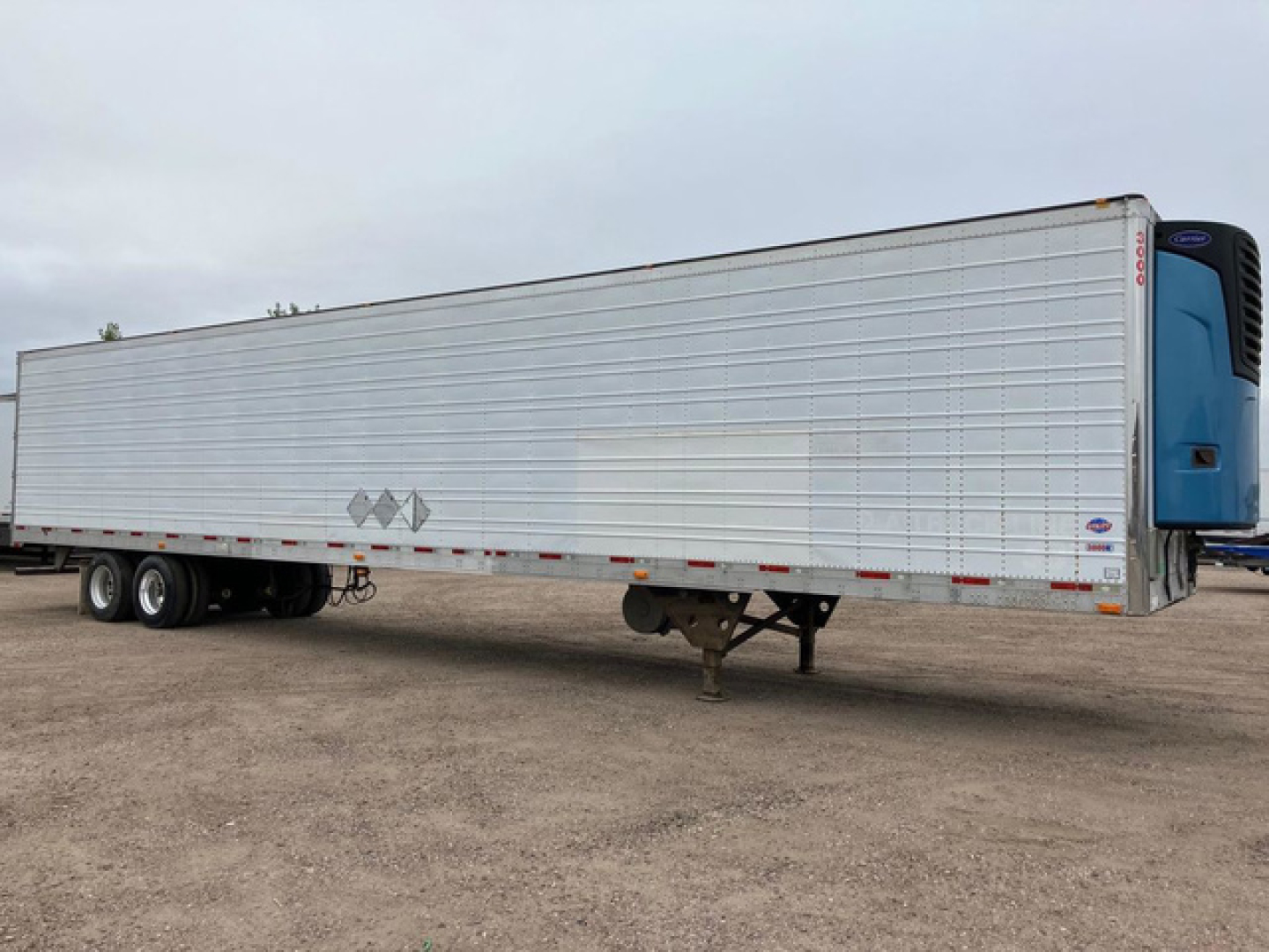 Trailer side view showing refrigerated utility trailer with aluminum side panels and blue cab-end.