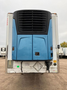 Refrigerated trailer rear view showing blue cooling unit and white rear doors with hazard placard.