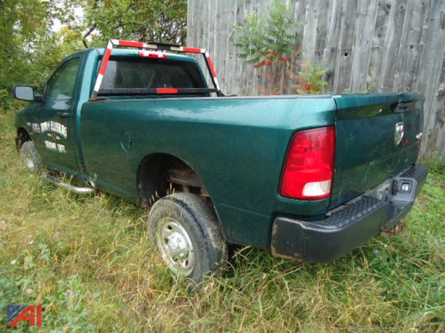 Ram 2500 pickup truck in green, rear-right view showing bed and taillights, with damaged wheel well and overgrown grass around the vehicle.