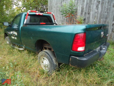 Ram 2500 pickup truck in green, rear-right view showing bed and taillights, with damaged wheel well and overgrown grass around the vehicle.