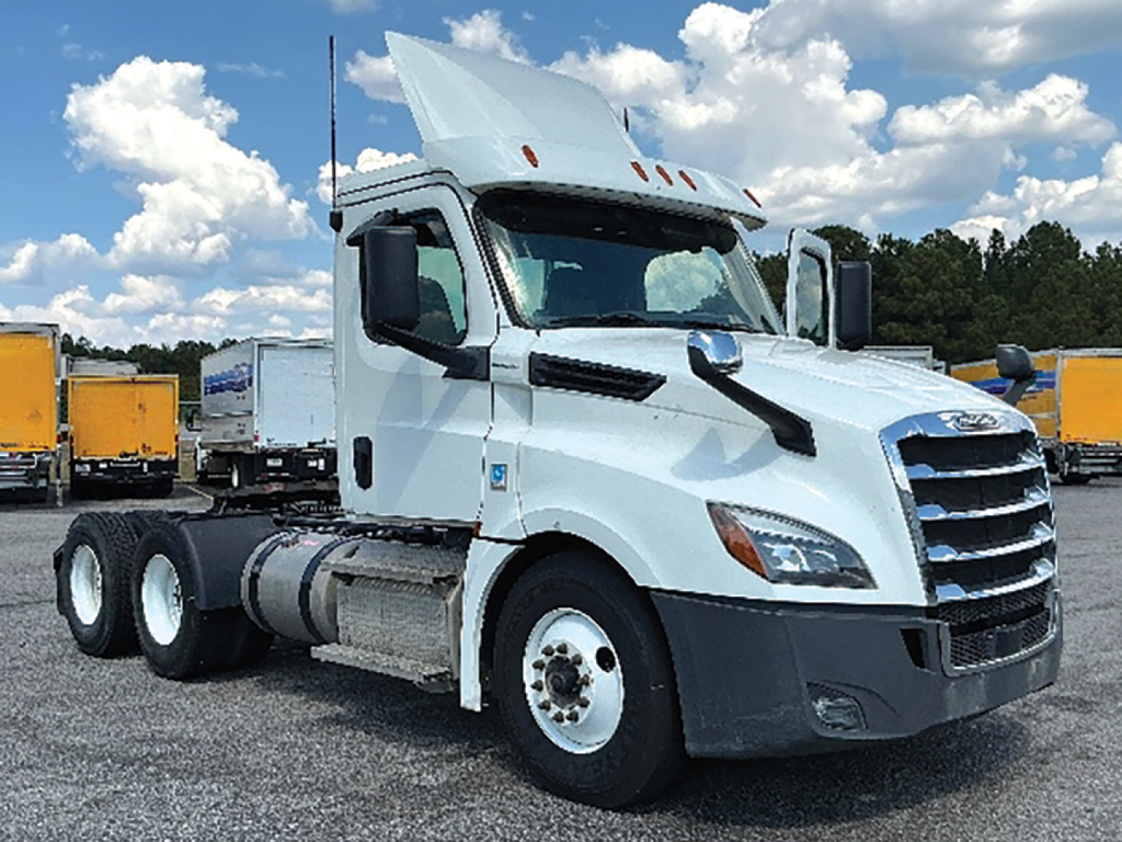 Truck cab with attached tractor chassis showing front and left side, Freightliner Cascadia 126, white exterior, cargo yard in background.