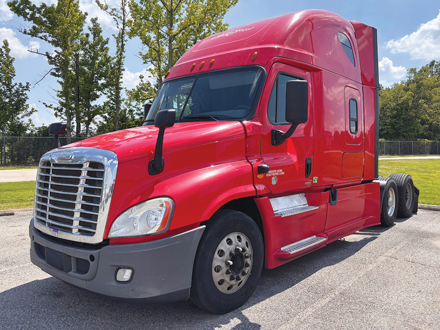 Red Freightliner Cascadia125 semi-truck cab in a dealership lot, front-right angle, chrome grille, large mirrors, two side steps, aerodynamic sleeper with windows.