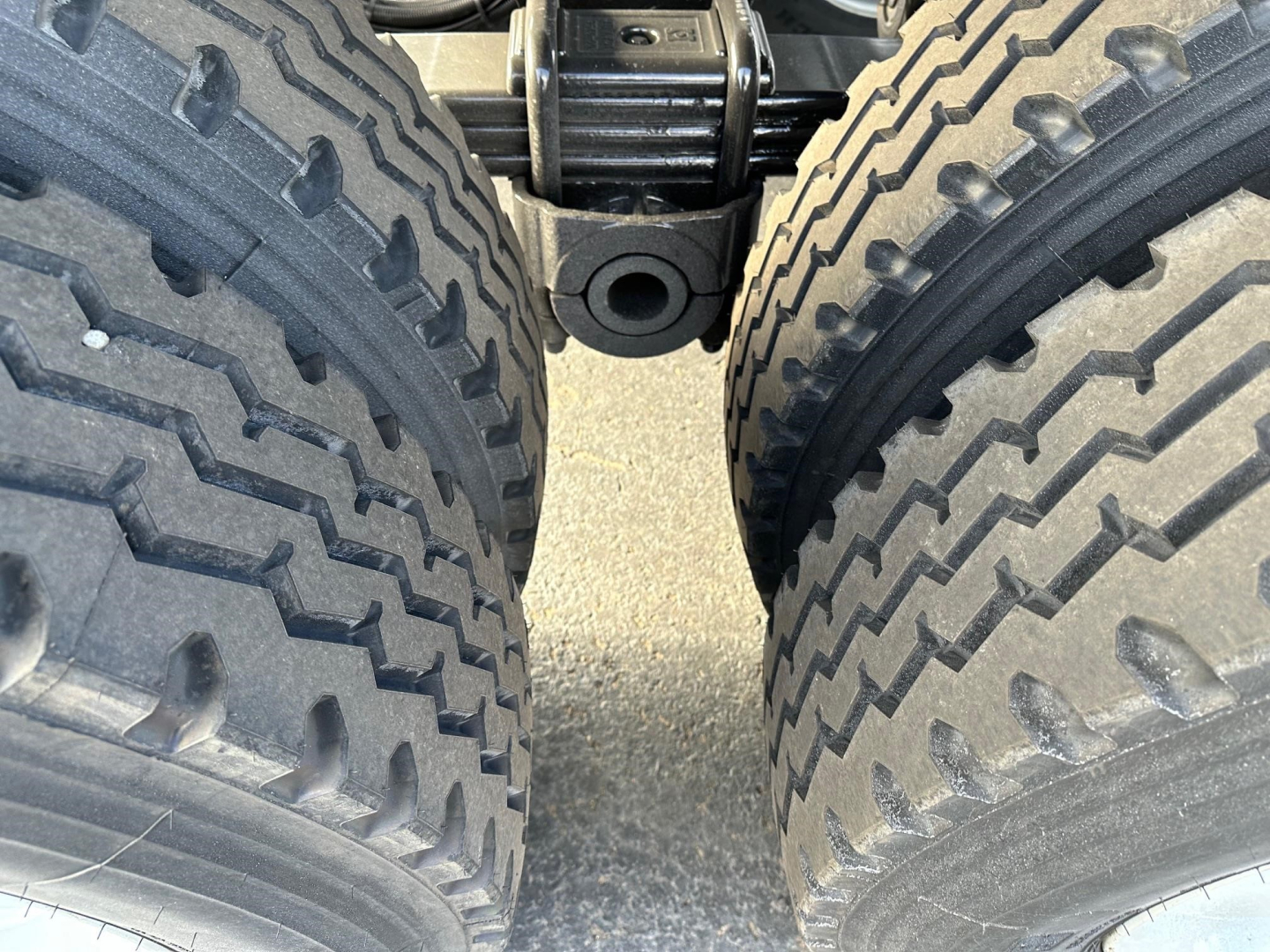 Close-up of dual rear tires on a dump trailer showing heavy tread, middle hinge area, and undercarriage components.