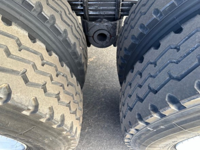 Dump trailer undercarriage view showing dual rear tires and axle center with hitch receiver. Visible treaded tires and connecting frame area.