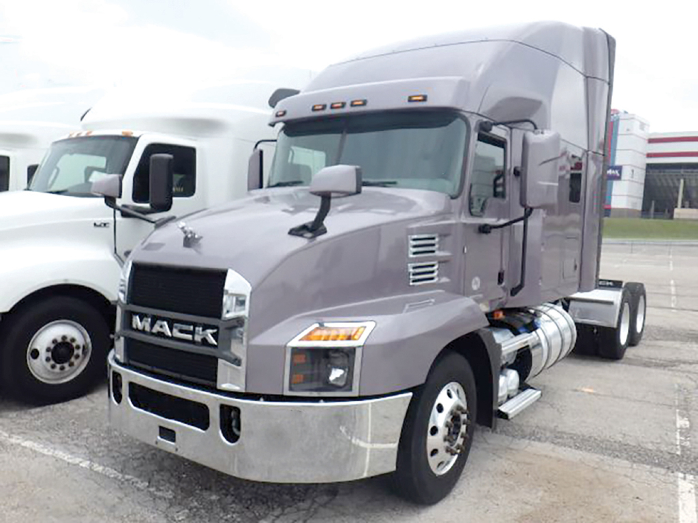 Mack Anthem truck in gray showings cab and front view with chrome bumper and side exhaust. Text on grille reads MACK.