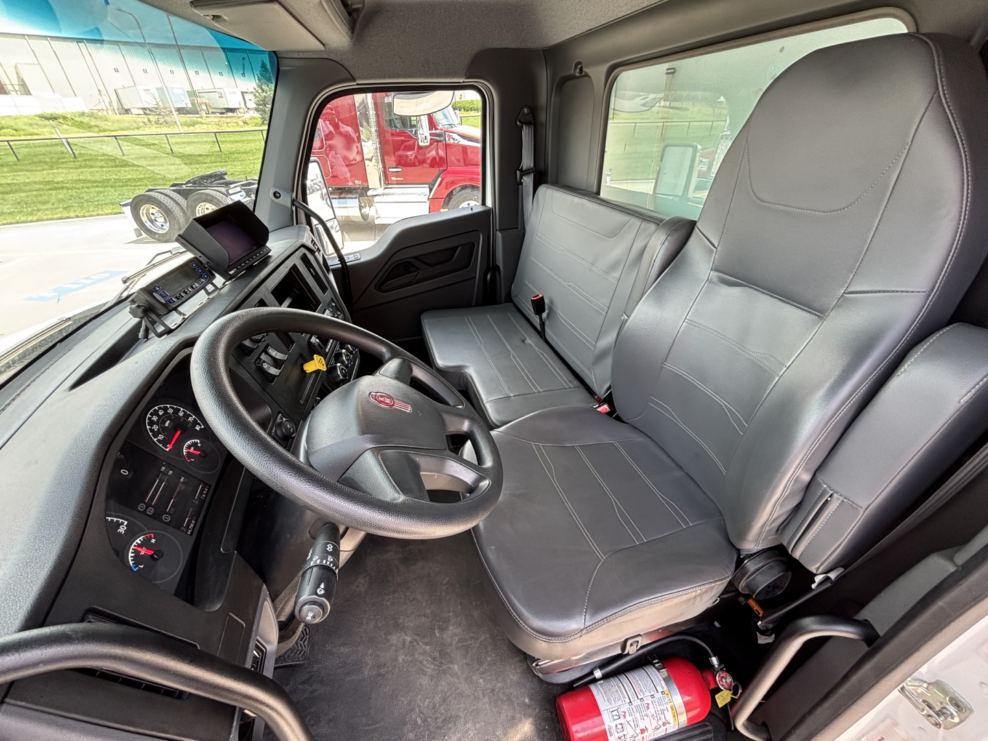 Kenworth T380 cab interior showing steering wheel, driver seat, passenger bench seat, dashboard with gauges and control stalks, sun visor, and door panel.