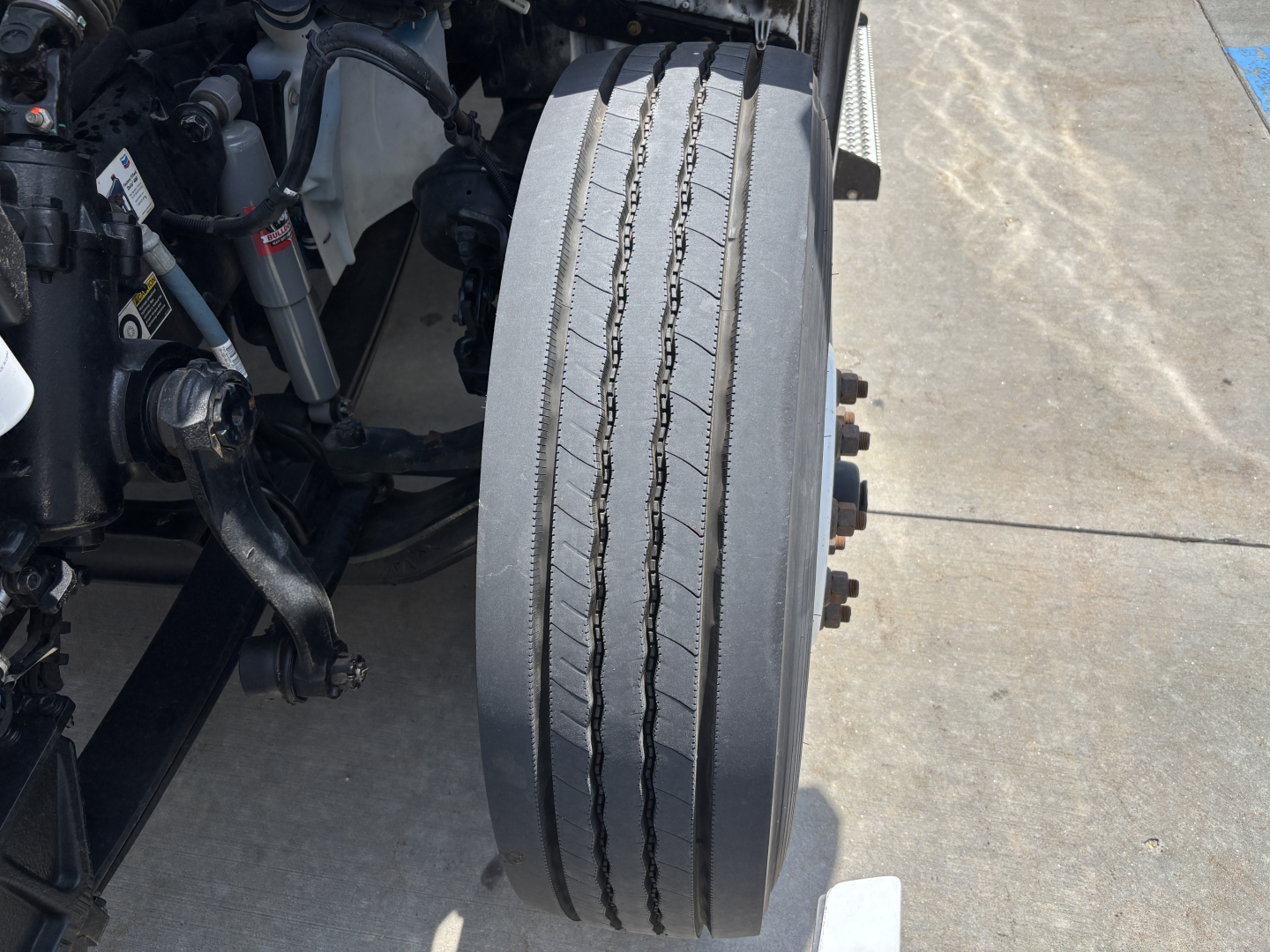 Truck wheel and suspension components of a Kenworth T380 front axle with dual tires and visible tire tread grooves.