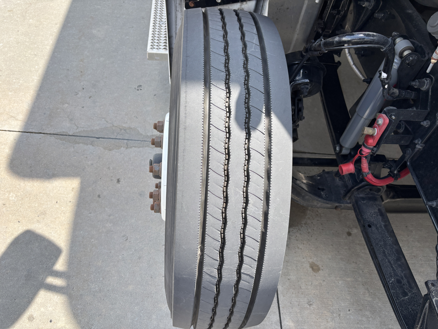 Kenworth T380 front wheel and suspension showing dual tires, wheel hub, and framing with hoses. No legible model text visible.