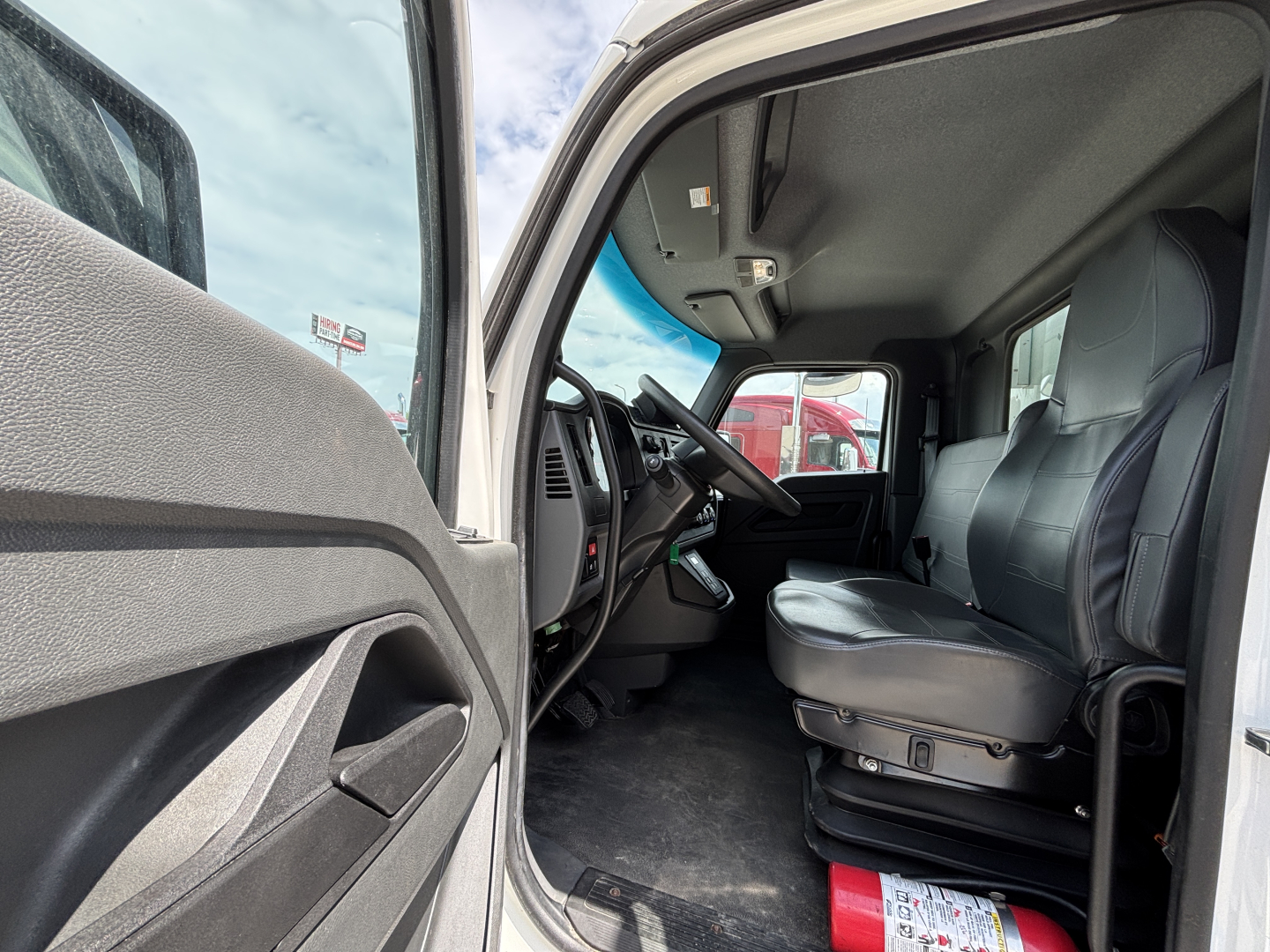 Kenworth T380 cab interior view from driver side door open showing driver seat steering wheel pedals and dashboard; part of refrigerated truck with gray interior.