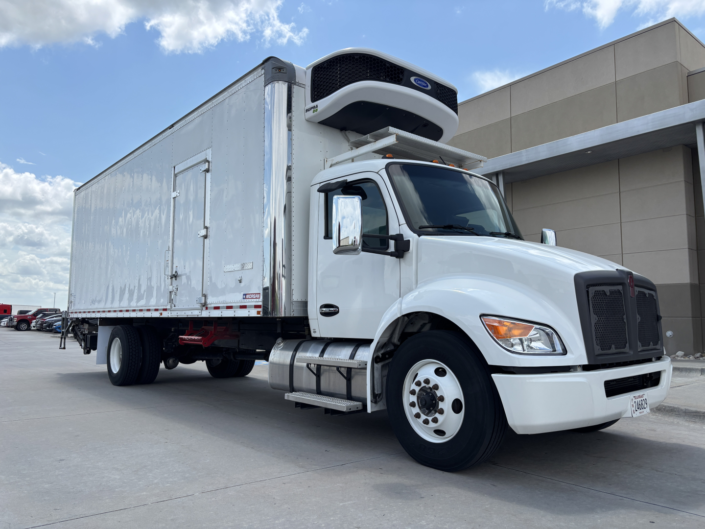 Truck engine bay and refrigerated body of a 2024 Kenworth T380 with a top-mounted Reefer unit, white cab, side mirrors, and cargo area in view.
