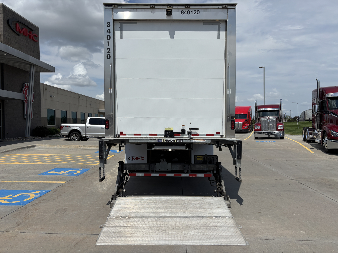 Kenworth refrigerated truck back view with liftgate deployed, white trailer doors, and blue handicap parking space lines in foreground.