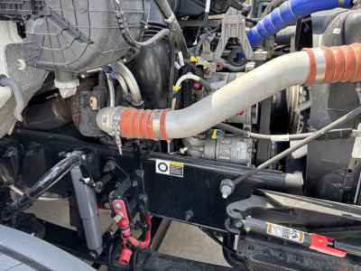 Kenworth T380 engine bay showing large intake hose and various hydraulic lines with orange clamps and a black mounting bracket.