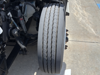 Truck wheel and suspension components of a Kenworth T380 front axle with dual tires and visible tire tread grooves.