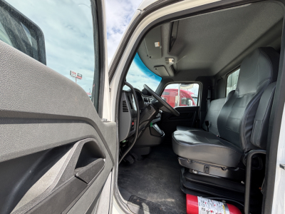 Kenworth T380 cab interior view from driver side door open showing driver seat steering wheel pedals and dashboard; part of refrigerated truck with gray interior.