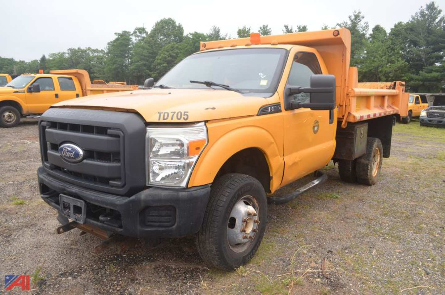 Ford F-350 Super Duty dump truck in orange, front-left view, TD705 badge on hood and dump bed visible, black grille, roadside lot.