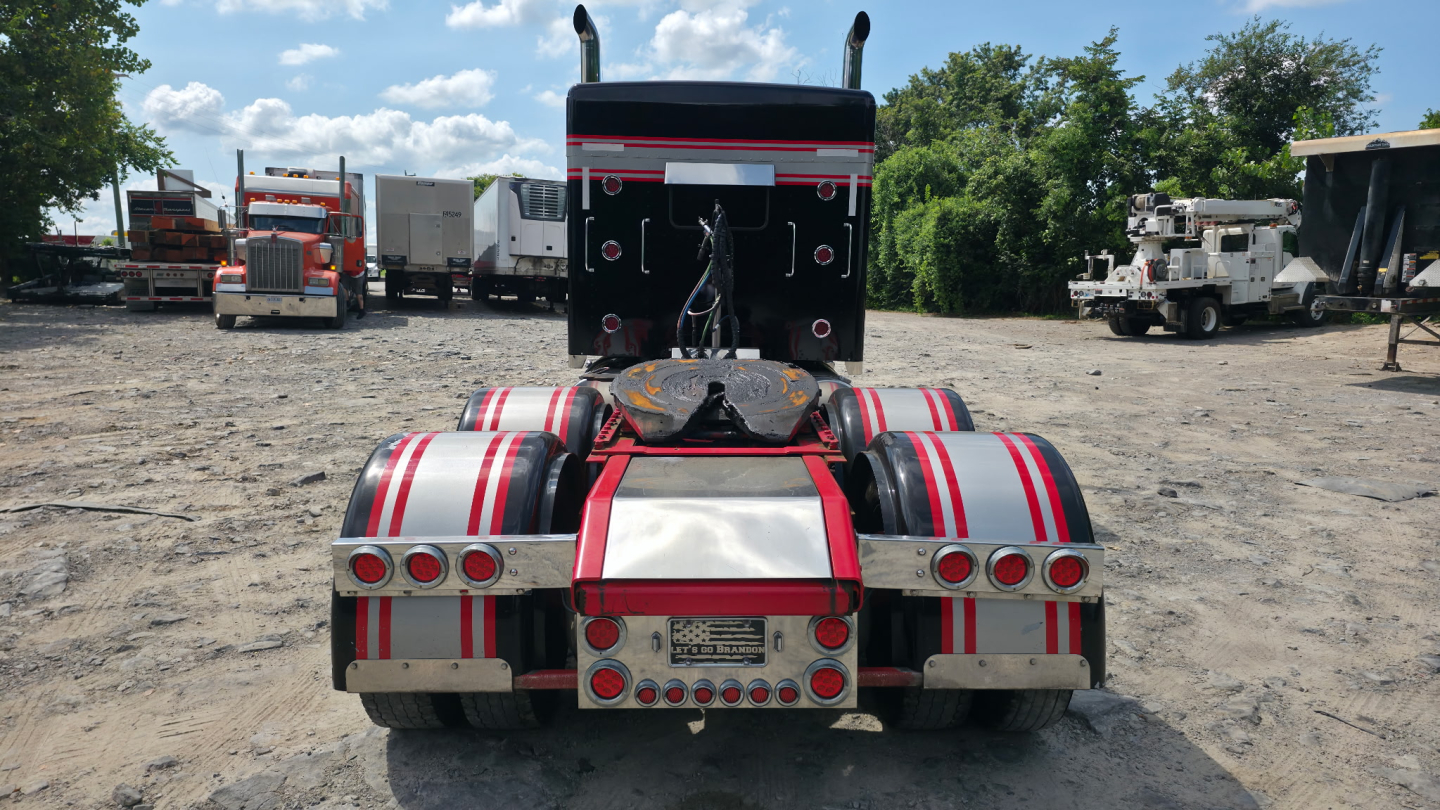Kenworth W900L tractor rear view showing dual rear axles with red-and-white reflective fender stripes and mounting hardware.