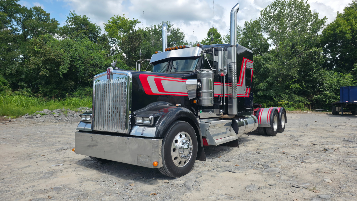 Kenworth W900L sleeper tractor with chrome grille, black and red paint, dual exhaust stacks, and dual rear axles.