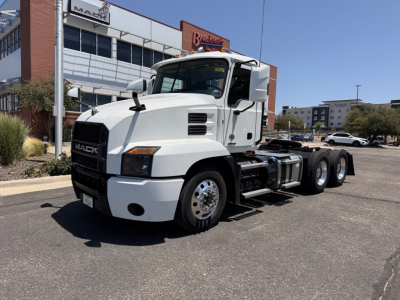 Truck in a dealership lot showing a white 2021 Mack Anthem daycab chassis with three rear axles, large mirrors, and black grille.