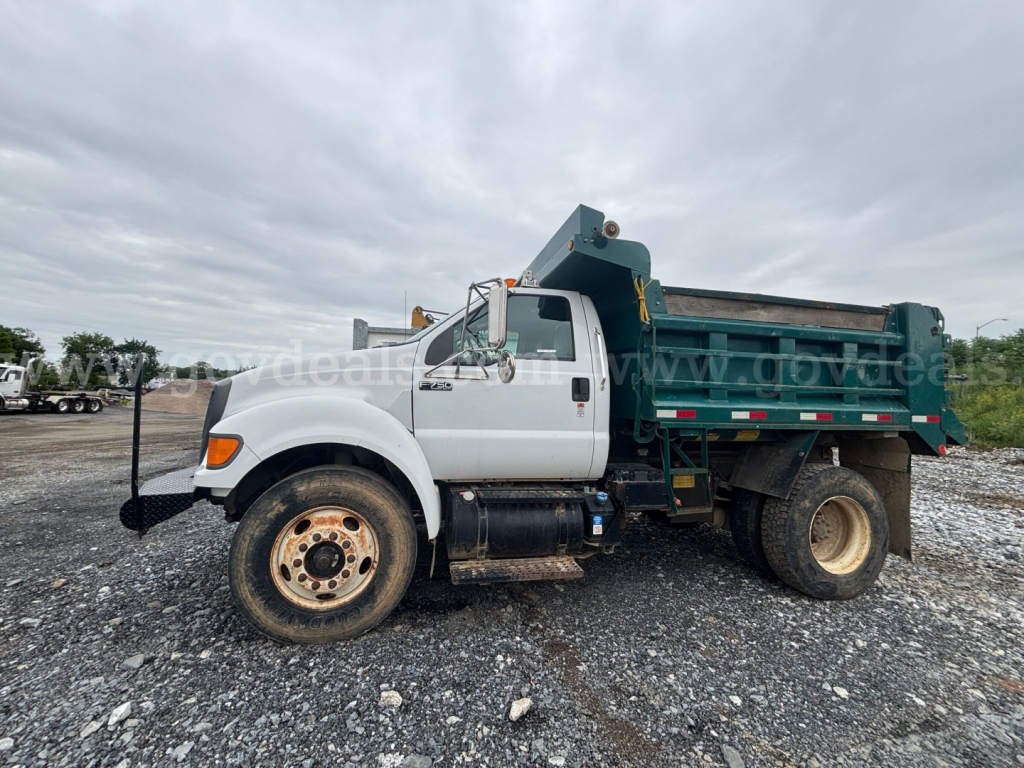 Ford F-750 dump truck side view showing white cab and green dump bed with black chassis and large rear wheels.