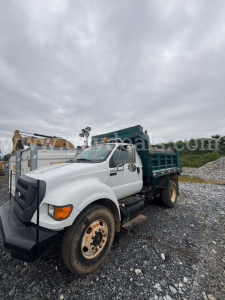 Ford F-750 dump truck in service showing front-left angle with white cab and green dump bed on a rocky lot
