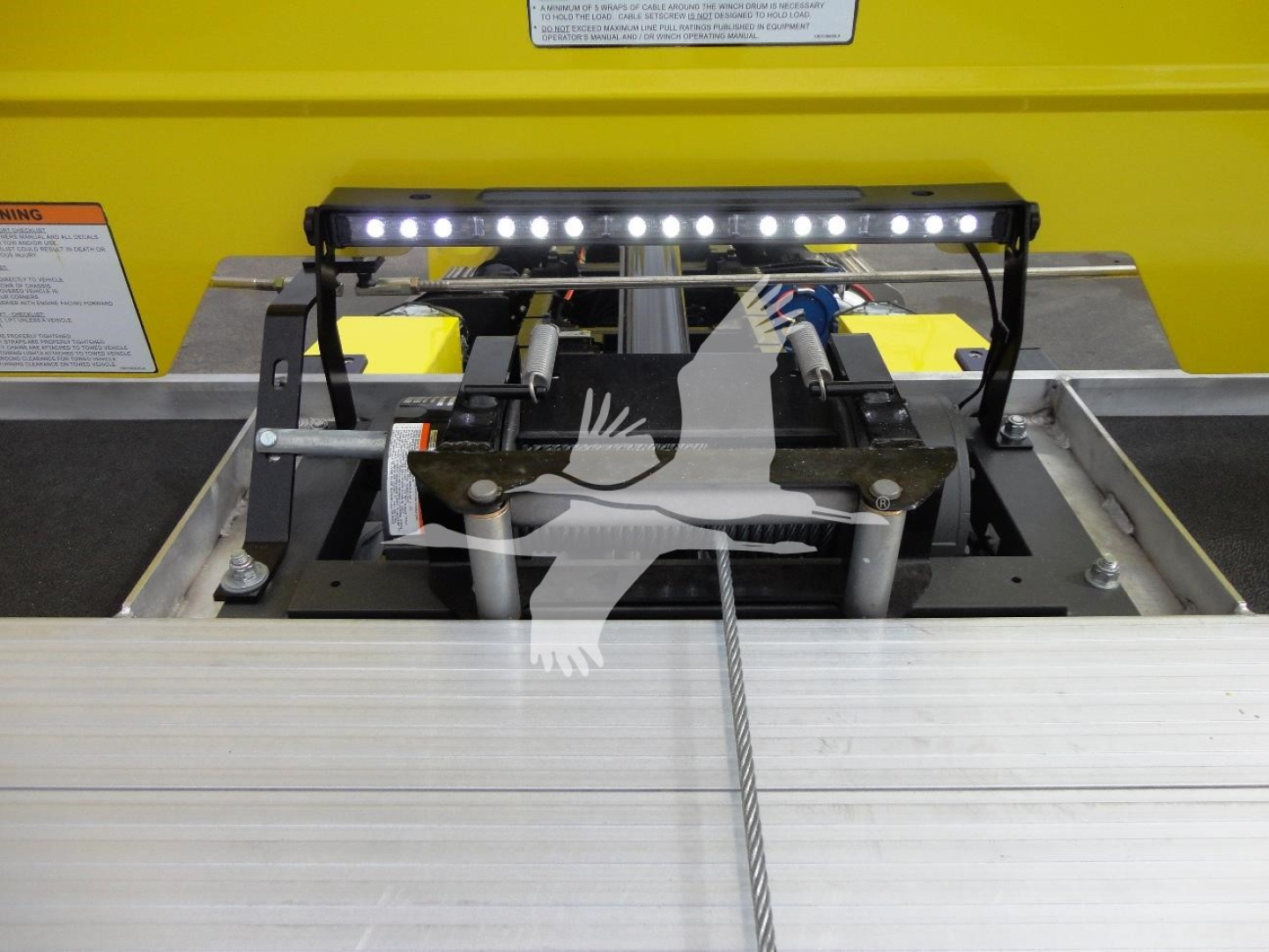 Truck bed winch assembly with LED light bar mounted above, cable and pulleys visible in foreground, yellow body in background.