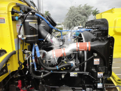 Peterbilt 337 engine bay showing turbocharger, hoses, and wiring in yellow truck cab with blue coolant lines and orange hose clamps.