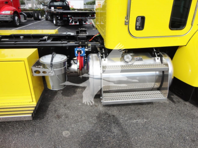 Peterbilt 337 rollback truck side showing stainless steel fuel tank with ladder steps and yellow cab; visible components include a silver cylindrical tank, connection lines, and a platform step.