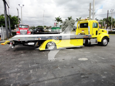 Peterbilt 337 rollback tow truck in yellow with flatbed, side view showing cab and flatbed in a dealership lot.