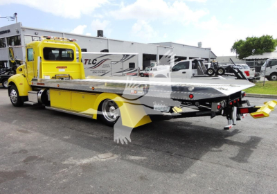 Peterbilt 337 rollback tow truck in yellow with flatbed, side view showing rear equipment and towing apparatus.