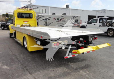 Peterbilt 337 rollback tow truck with yellow cab and long flatbed, rear view shows diamond plate bed and rear control ramps.