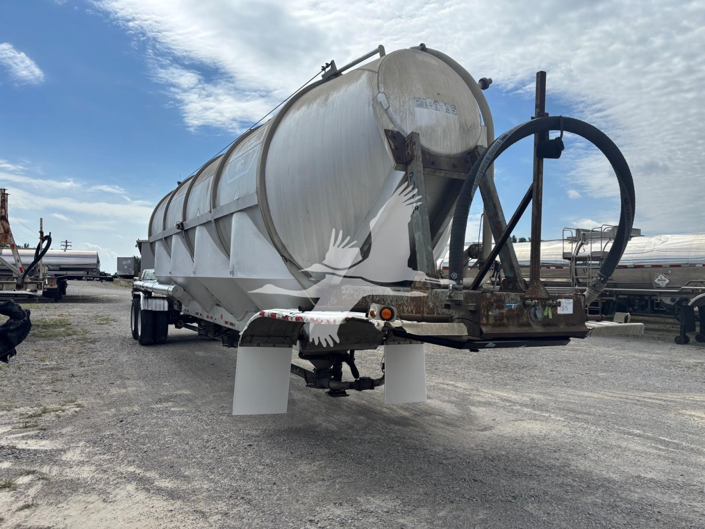 Pneumatic dry bulk trailer with cylindrical steel tank on trailer, rear discharge pipe and support legs visible.