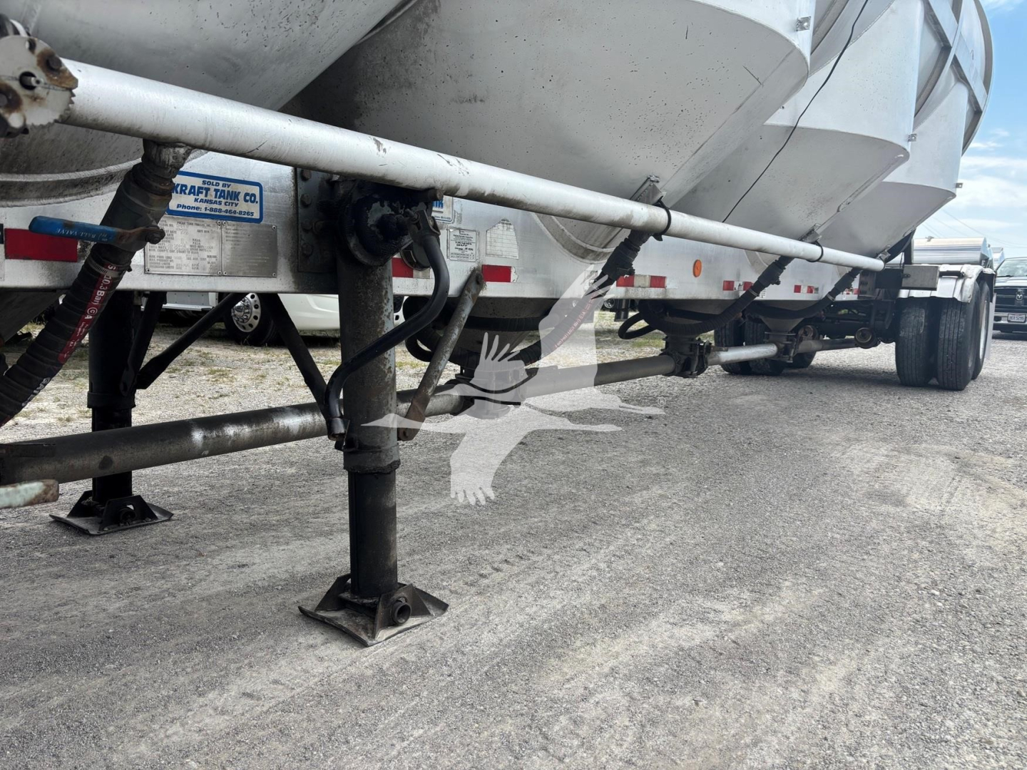 Trailer undercarriage with landing legs and support beam visible; some labels on the side include a blue sticker with text and a white label.