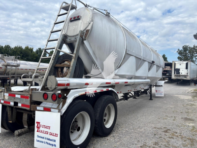 Pneumatic dry bulk trailer showing cylindrical aluminum tank on tandem axle with rear ladder and red/white reflective stripes.